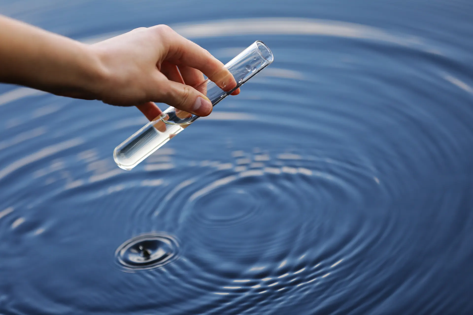 A trusted water storage solution you can depend on Hand holding a test tube of water sample above rippling water